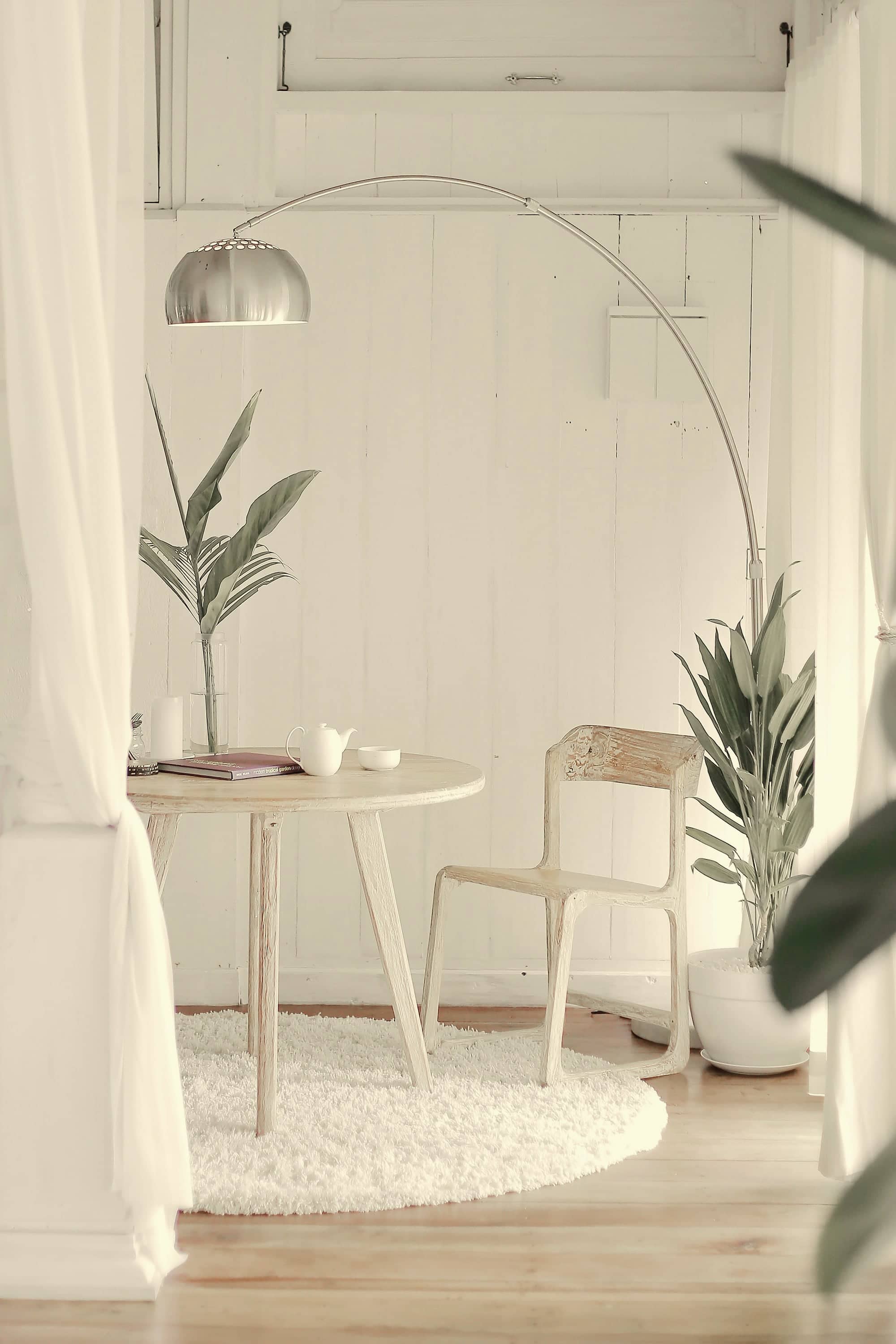 Un coin d'attente lumineux : table ronde en bois clair, chaise, plantes et voilage blanc.