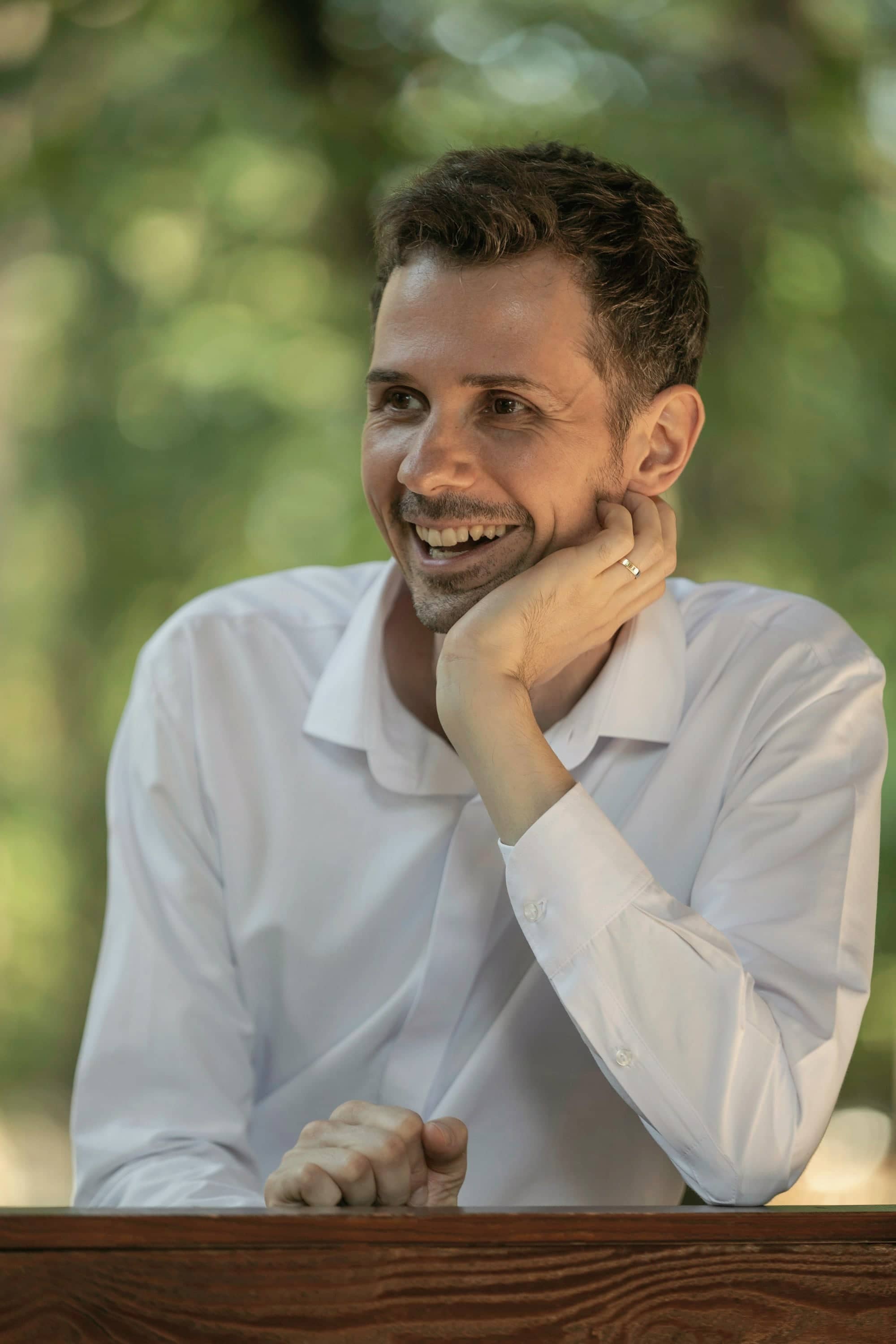Camille Verdier, souriant, en chemise blanche, accoudé à une table en bois.